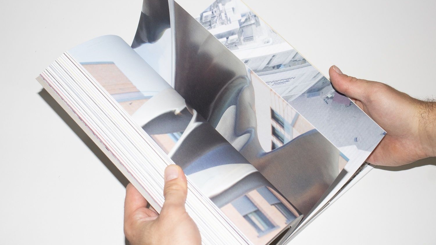 Zwei Hände halten einen Katalog, der Fotografien von Kunstwerken zeigt.